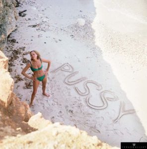 English actress Honor Blackman on a beach for a publicity shot for the 1964 James Bond 'Goldfinger'. Spelt out in the sand is the name of her character, Pussy Galore.